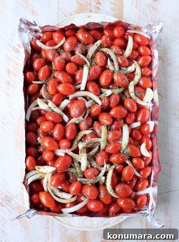 cherry tomatoes, onions and garlic on a foil lined baking sheet