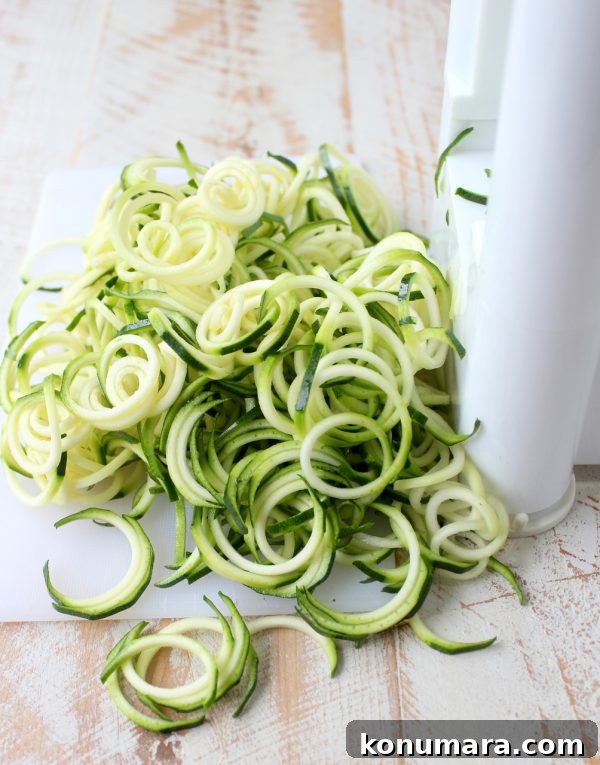 zucchini noodles coming out of a spiralizer on a white wood board
