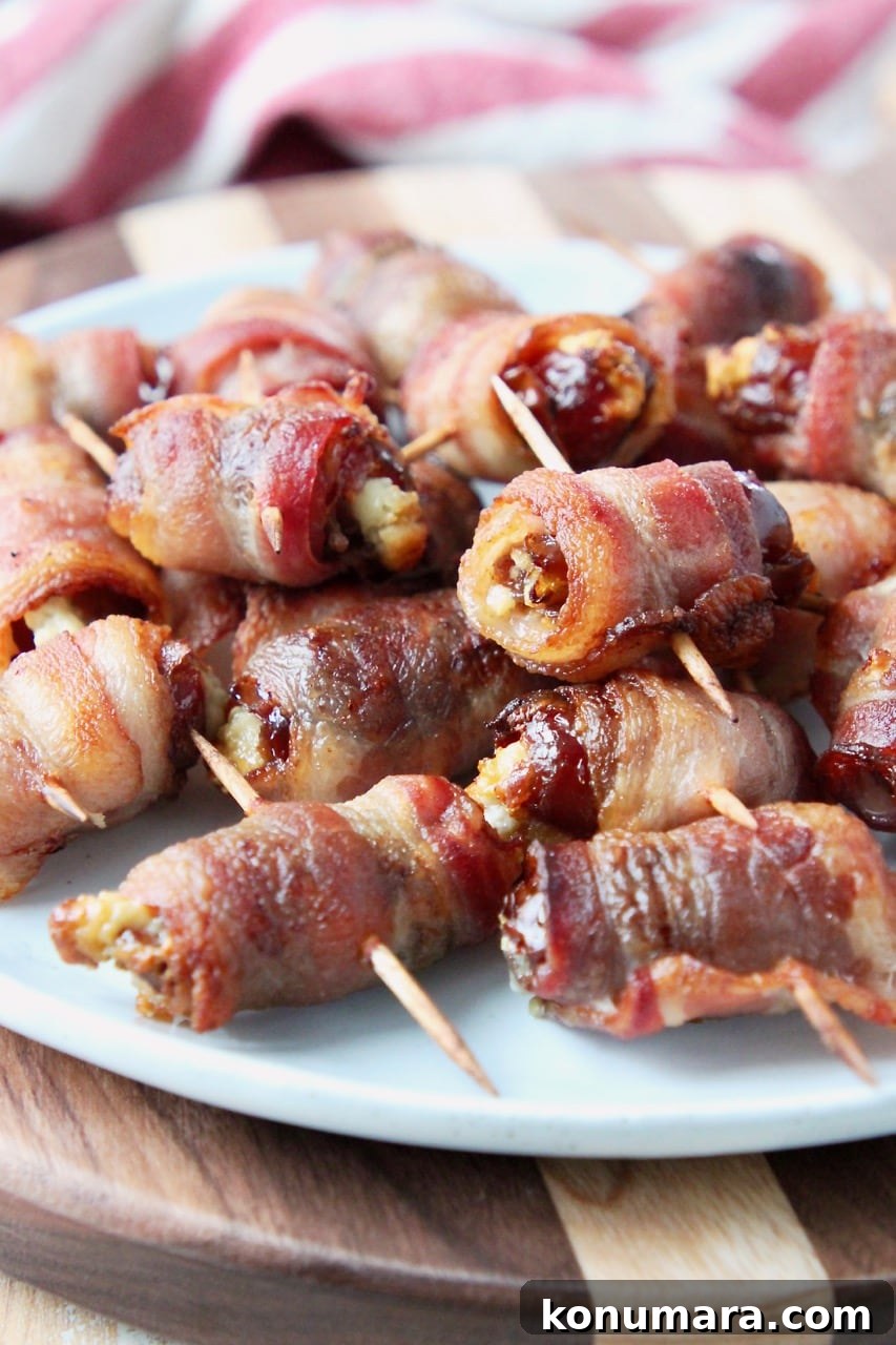 Bacon-Wrapped Dates Appetizer Recipe 2 Bacon wrapped dates piled up on white plate on top of wood cutting board