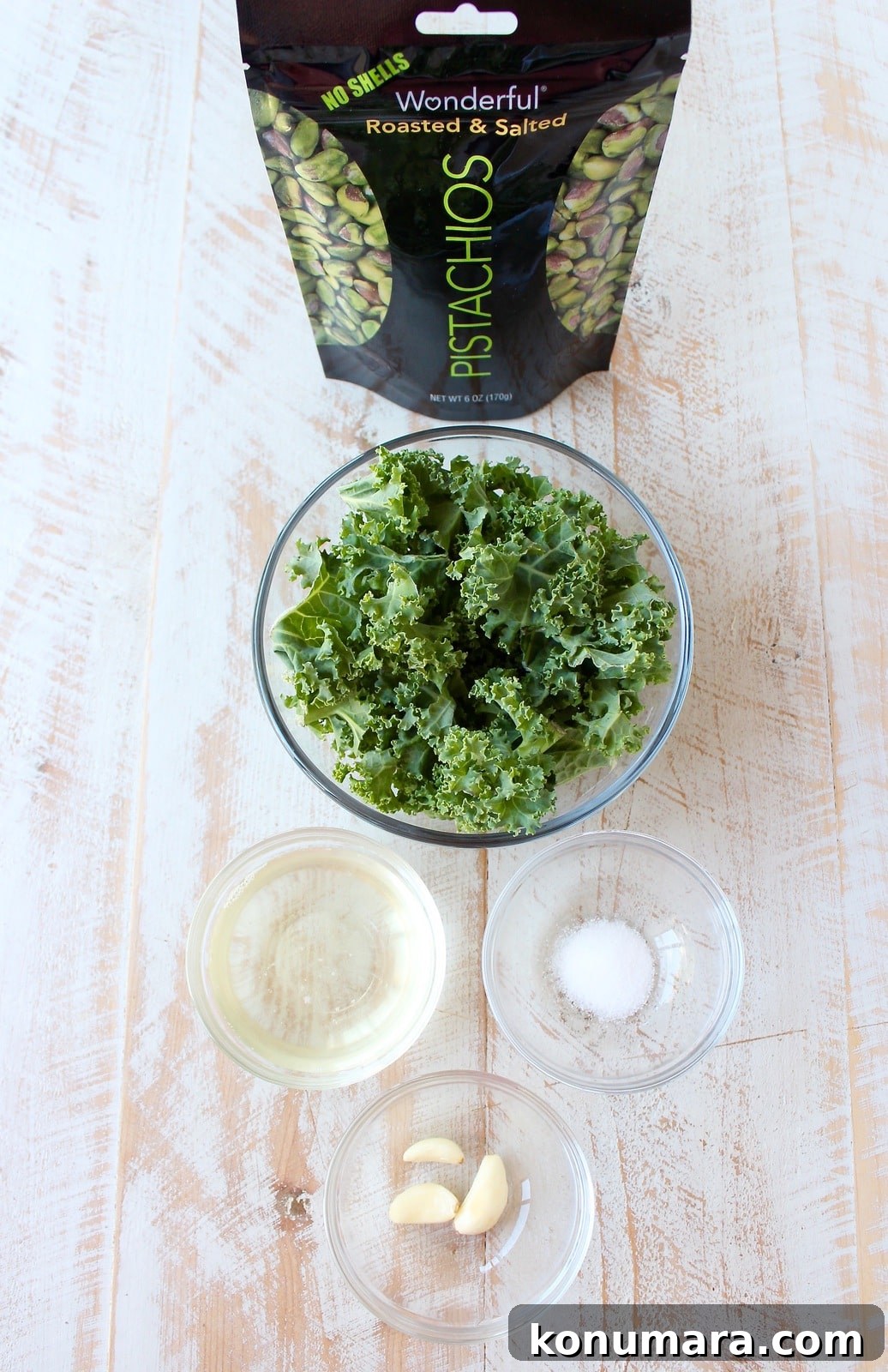 ingredients for kale pistachio pesto on a white wood board