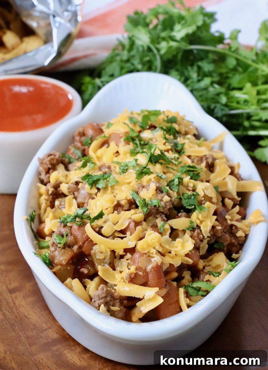 frito chili pie in small white dish topped with shredded cheddar cheese