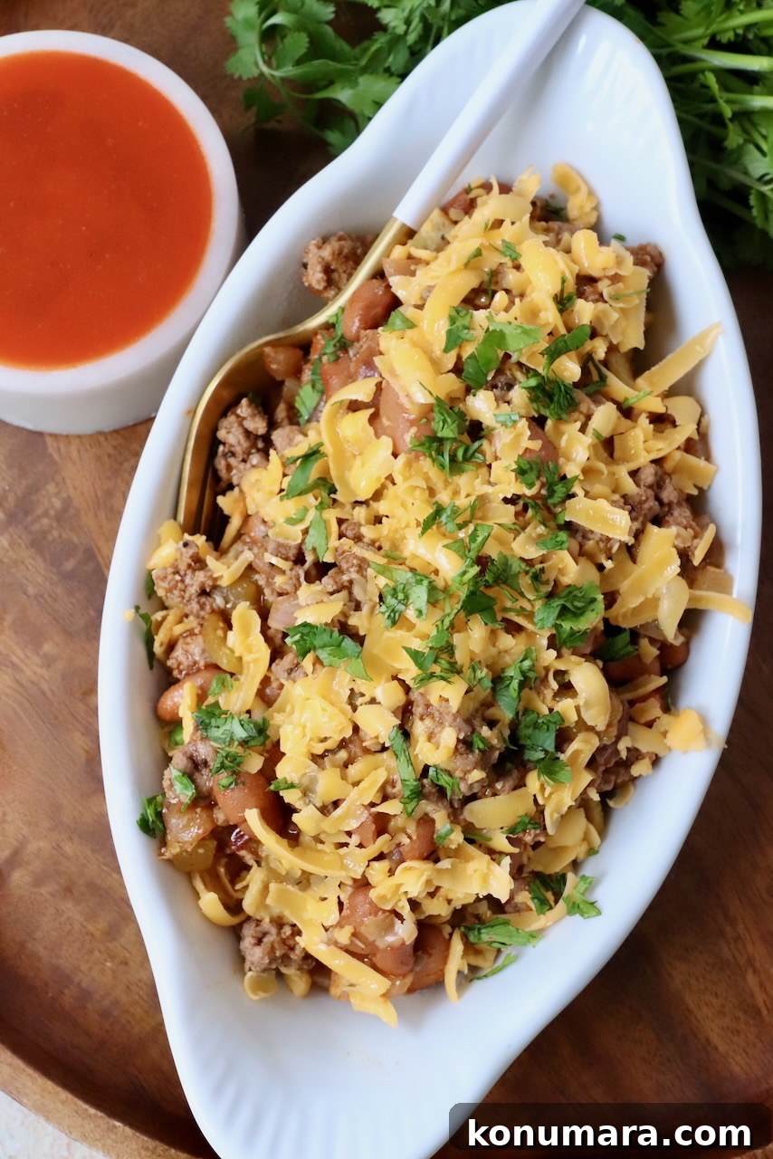 frito chili pie topped with shredded cheddar cheese in small white dish
