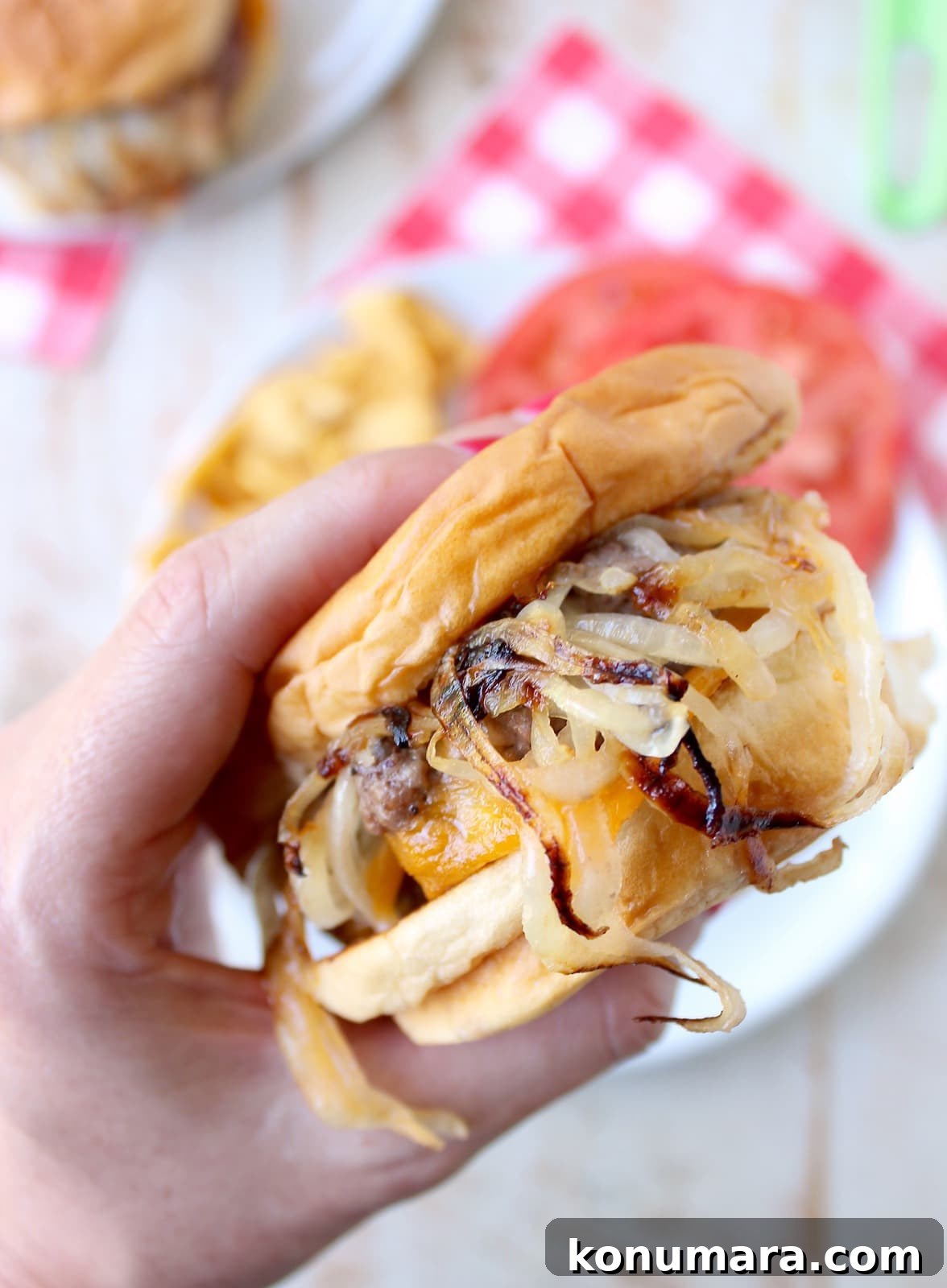 hand holding an onion fried burger above a plate