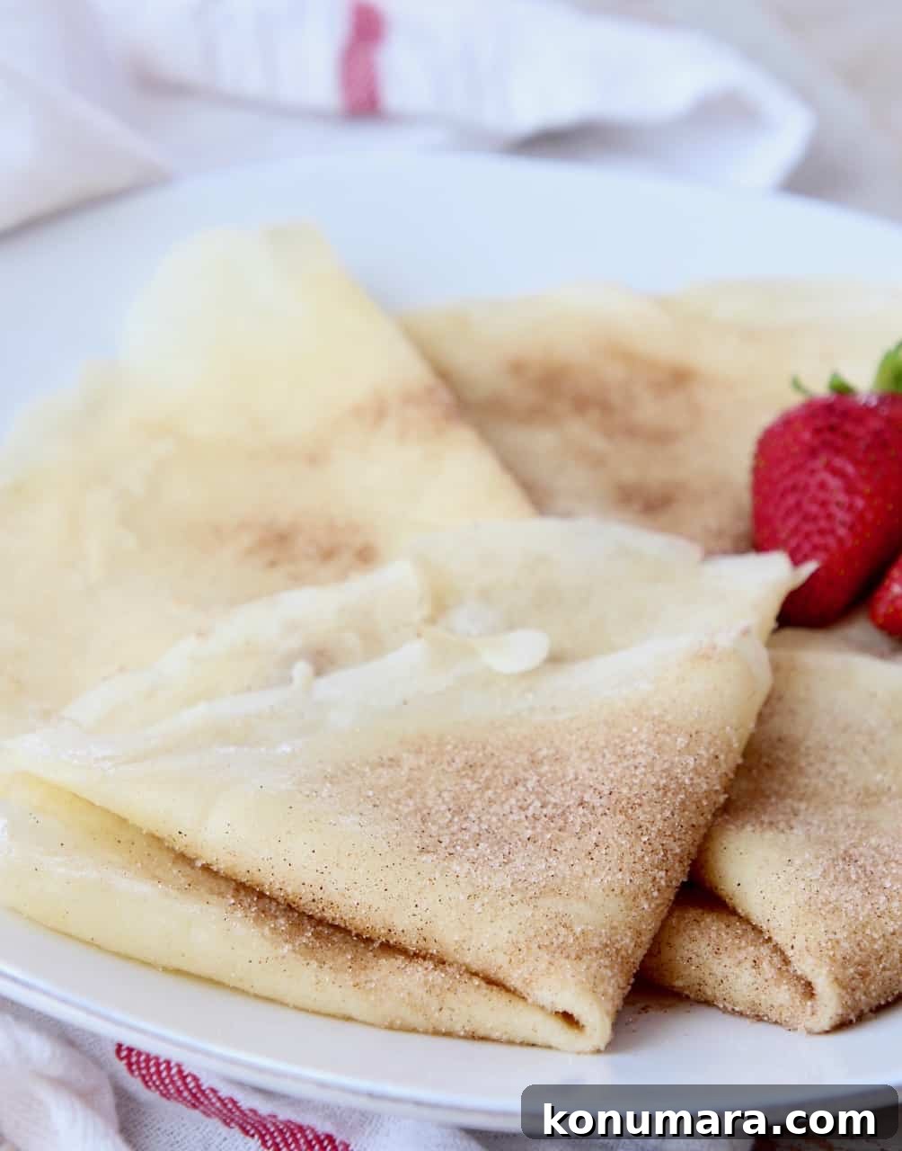 Classic French Crepes Recipe with Sweet and Savory Fillings 5 cinnamon sugar crepes folded on plate with strawberries