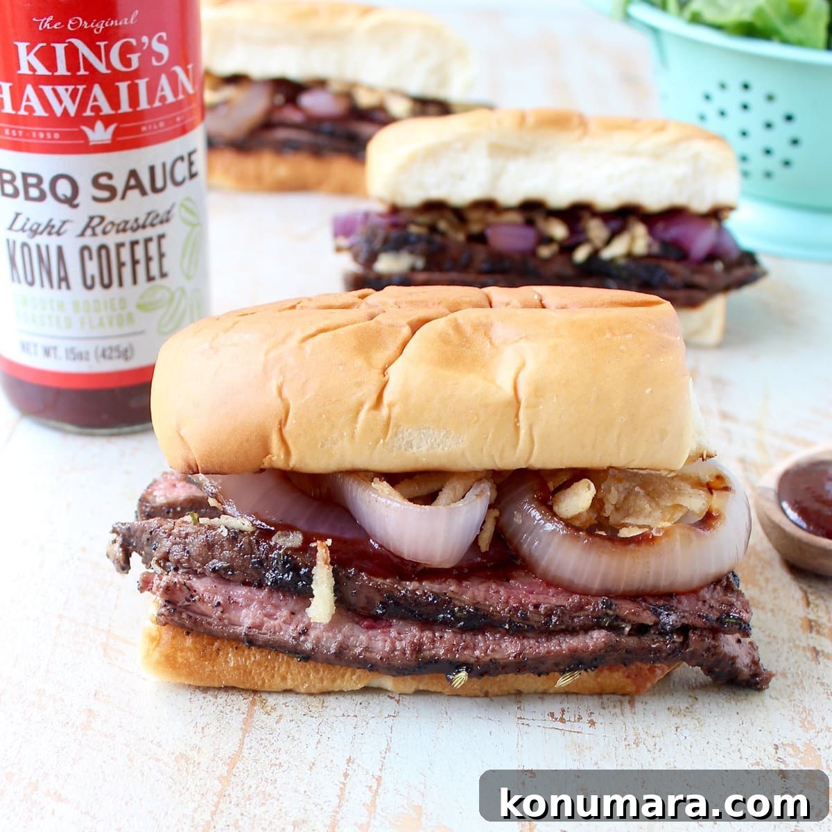 steak sandwiches on white wood board with bottle of bbq sauce in the background