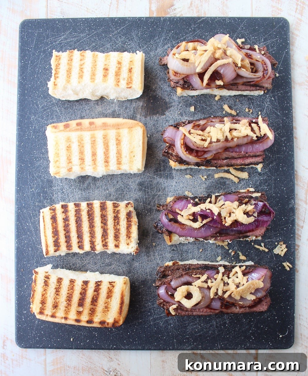 steak sandwiches on cutting board topped with grilled onions and crispy fried onions