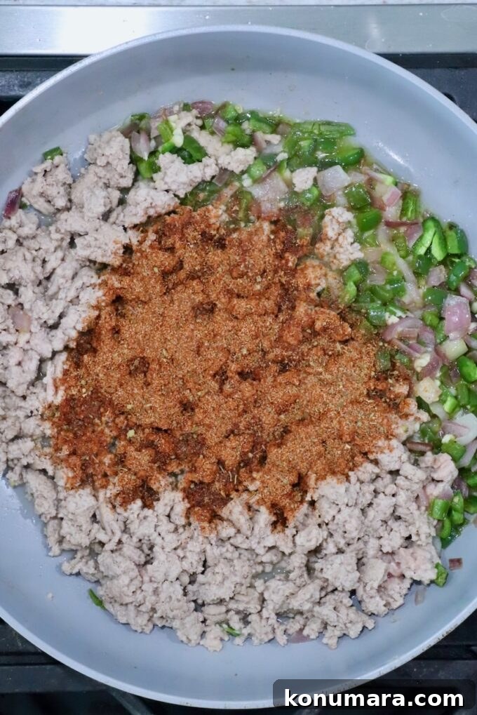 taco seasoning on top of cooked ground turkey and diced vegetables in a skillet