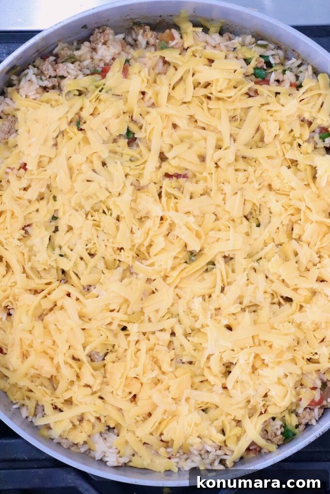 taco rice in a skillet topped with shredded cheddar cheese