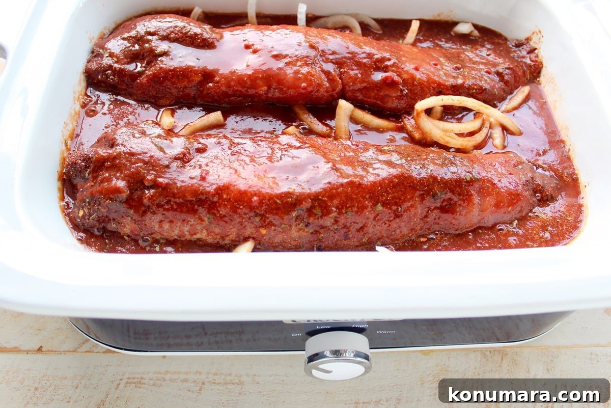 Two pork tenderloins in a slow cooker covered with sauce.
