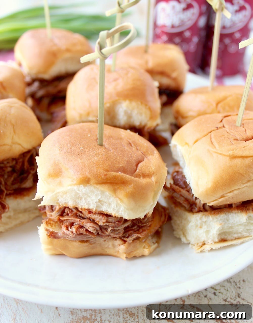 Mini pulled pork Hawaiian roll sandwiches on a white plate with a toothpick in each one.