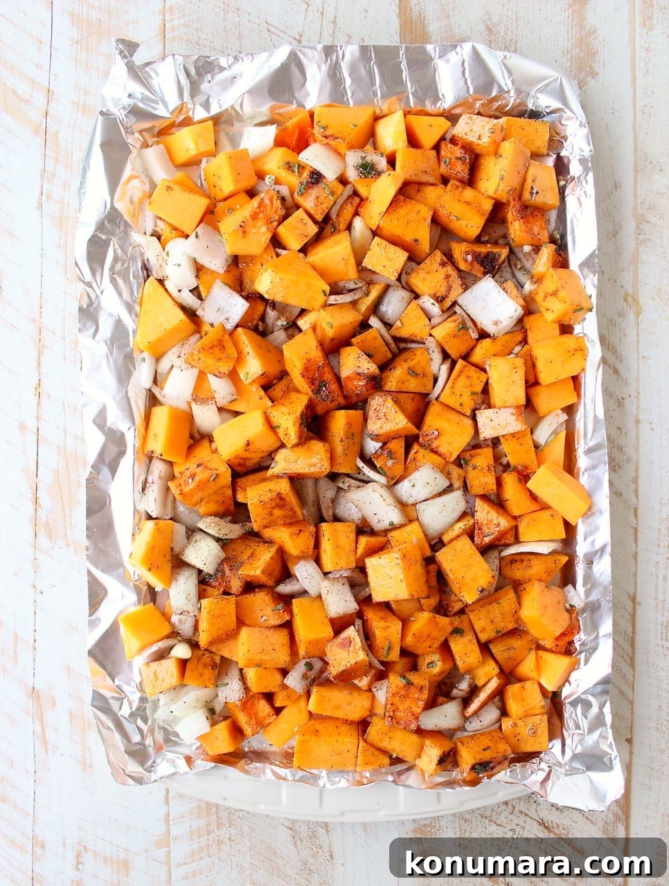 Roasted butternut squash and onions seasoned on a foil-lined baking sheet