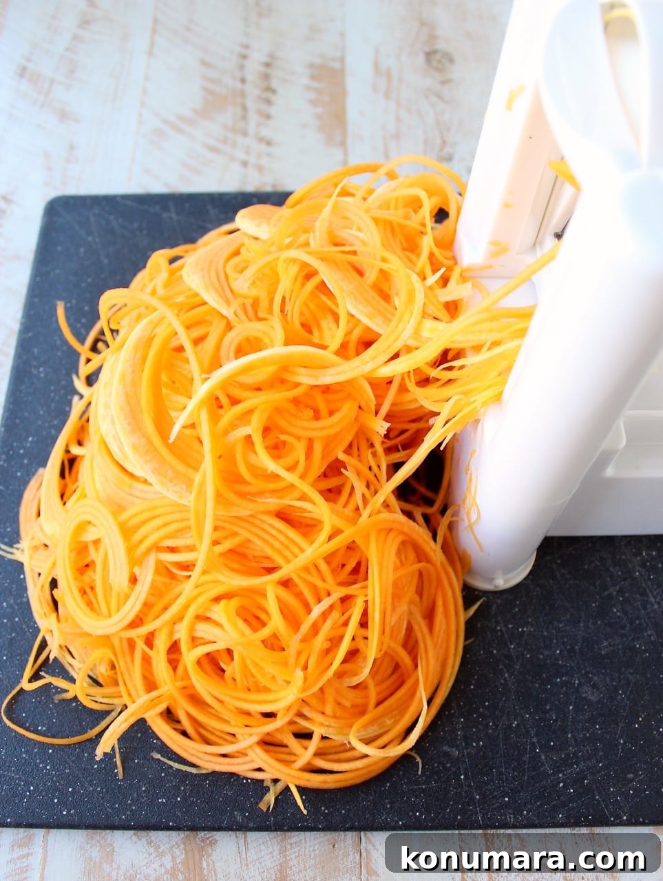butternut squash noodles coming out of a spiralizer machine onto a cutting board