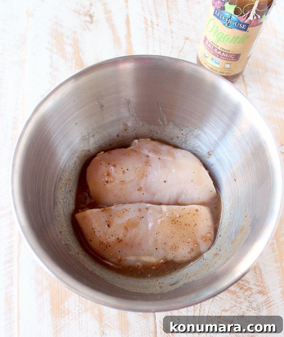 raw chicken breasts covered in balsamic vinaigrette dressing in a metal bowl