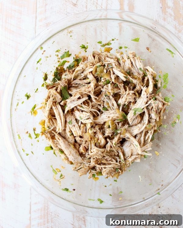 cooked shredded chicken tossed with green chilies and seasonings in glass bowl
