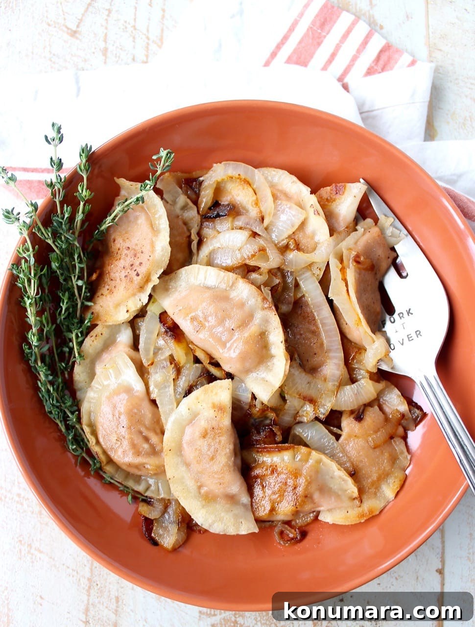 Sweet Potato Pierogi Recipe with Caramelized Onions 2 cooked pierogies and caramelized onions in an orange bowl with fresh thyme