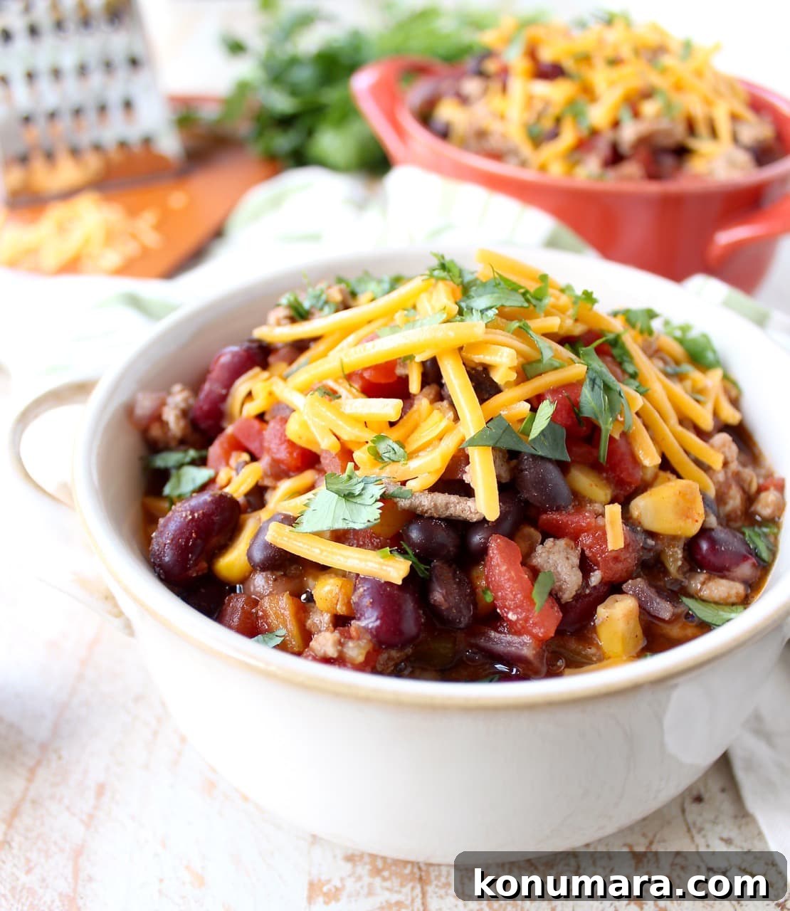 A white bowl filled with taco soup topped with shredded cheese and herbs.