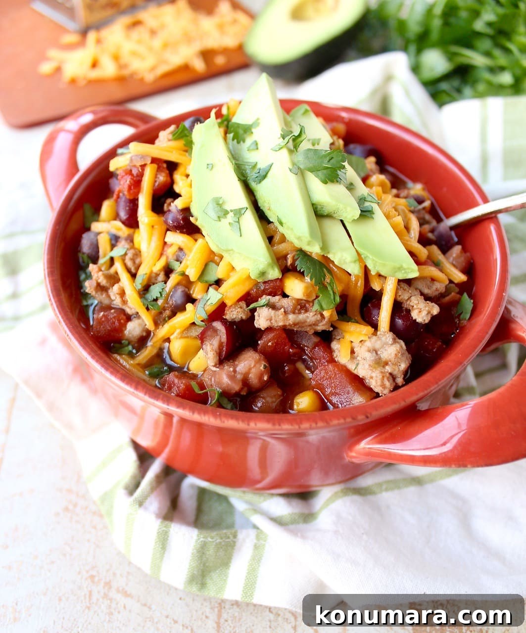 A red bowl filled with turkey taco soup topped with shredded cheese and avocado. 