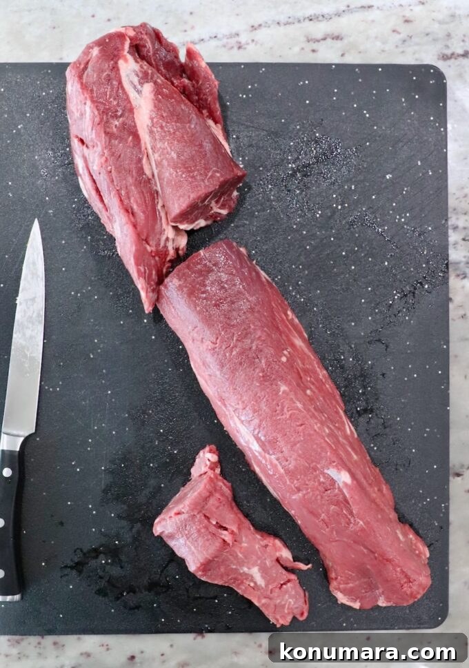 beef tenderloin cut into three sections on a cutting board with a knife