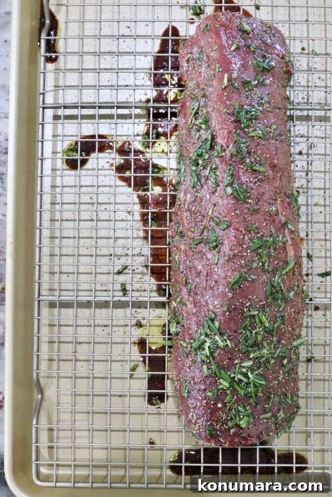 herb rubbed beef tenderloin on a wire rack over a rimmed baking sheet