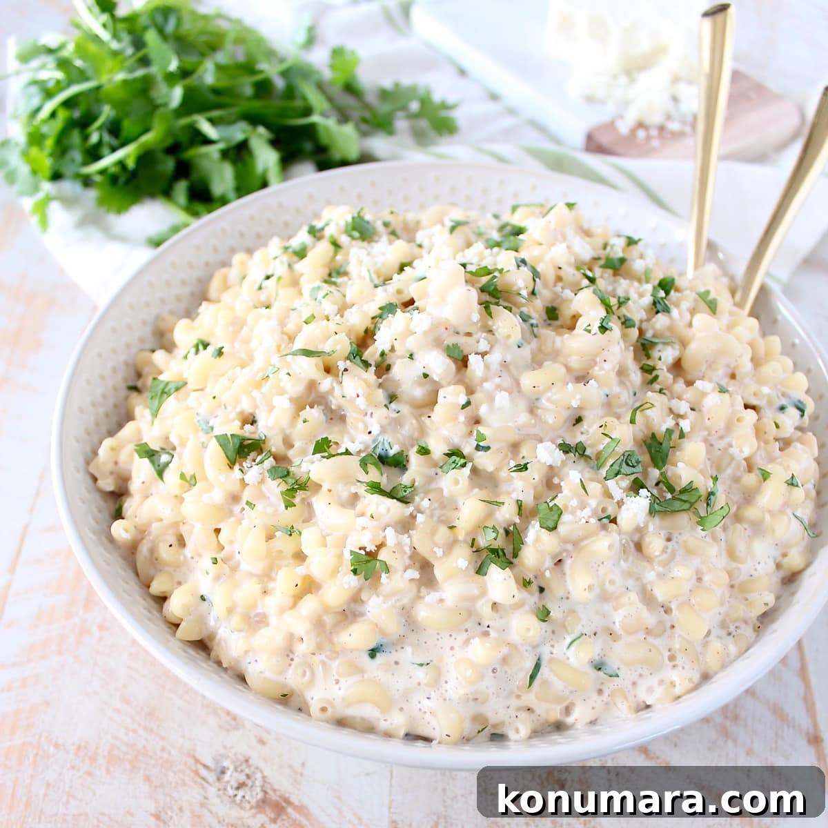 Mexican street corn mac and cheese in a white bowl with gold serving spoons. 