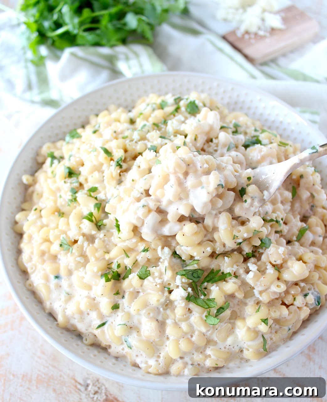 Mexican street corn mac and cheese in a white bowl with green herbs in the background. 