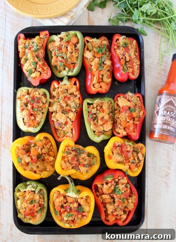 Overhead shot of buffalo chicken stuffed bell peppers on baking sheet with bottle of buffalo sauce on the side