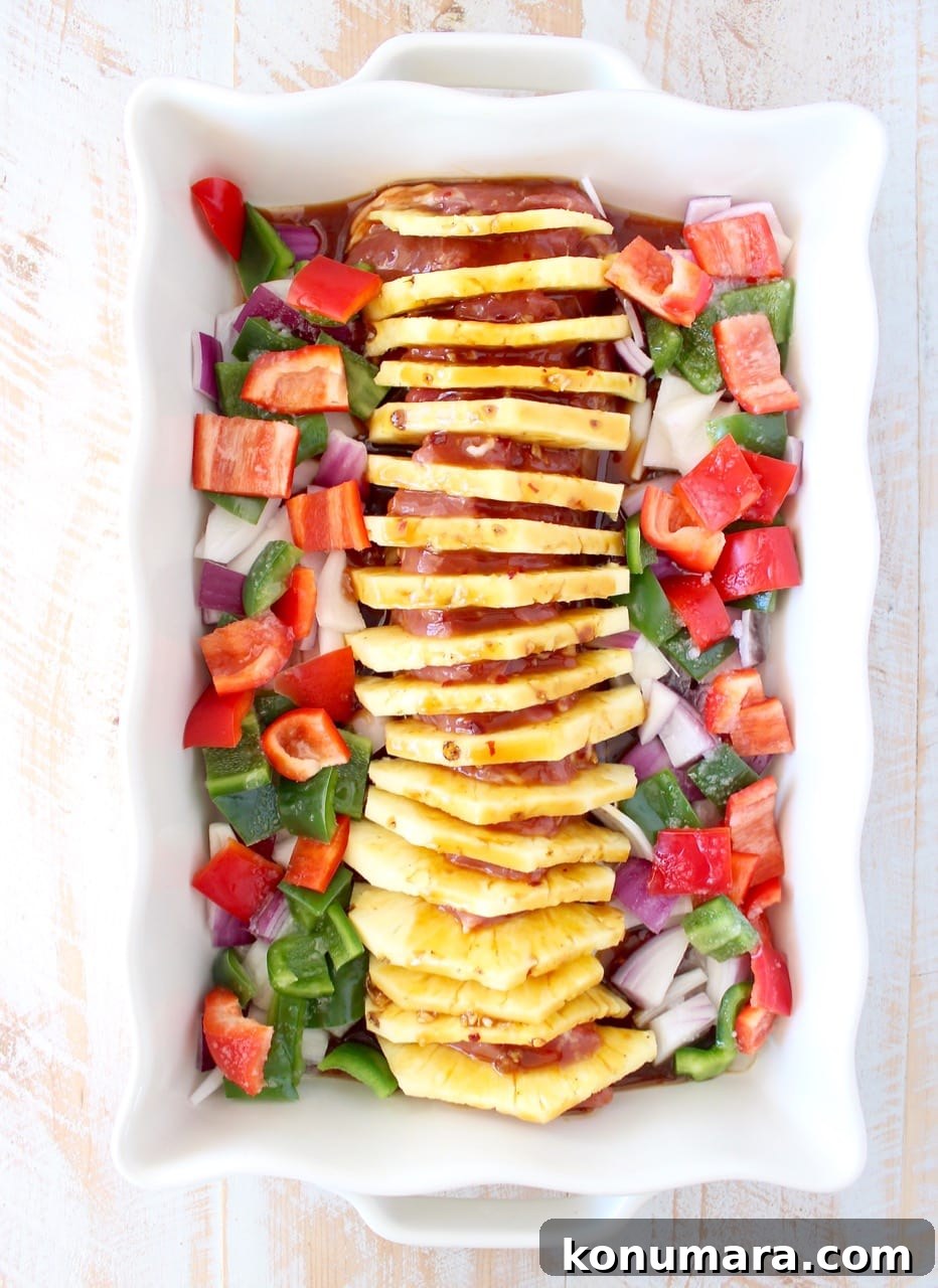 Glazed Pineapple Teriyaki Pork Tenderloin Recipe 3 uncooked pork tenderloin filled with slices of pineapple in a baking dish surrounded by diced bell peppers and onions