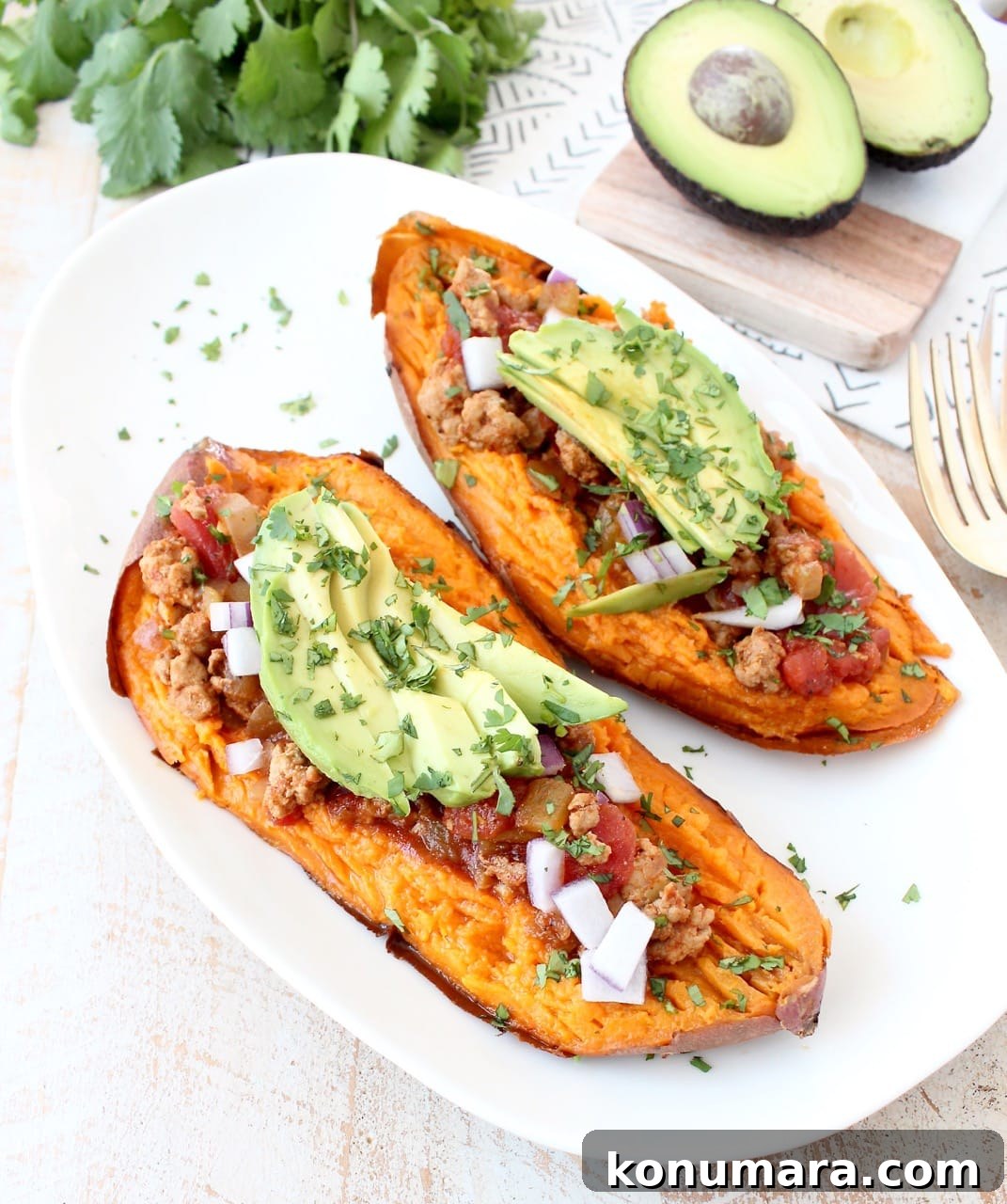 Smoky Chipotle Chili Stuffed Sweet Potatoes Recipe 6 baked sweet potato sliced in half on white plate, topped with chili, avocado and cilantro