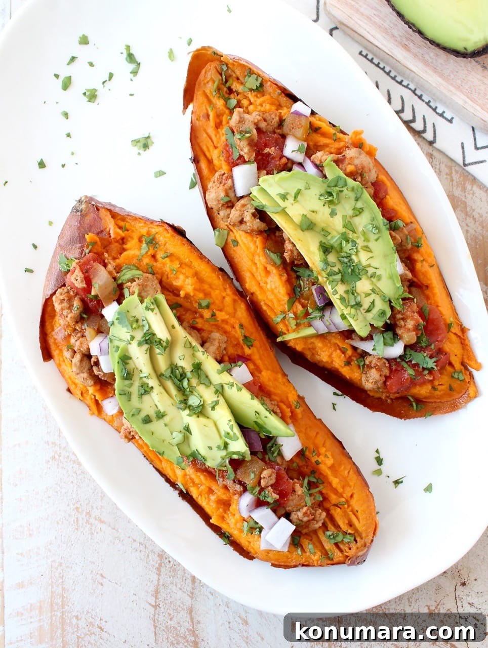 Smoky Chipotle Chili Stuffed Sweet Potatoes Recipe 7 baked sweet potato sliced in half on white plate, topped with chili, avocado and cilantro