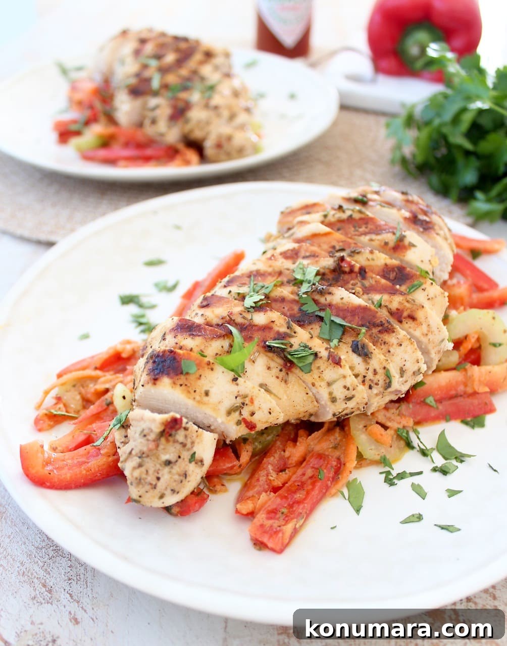 A white plate topped with sliced red bell peppers and a sliced chicken breast garnished with herbs.