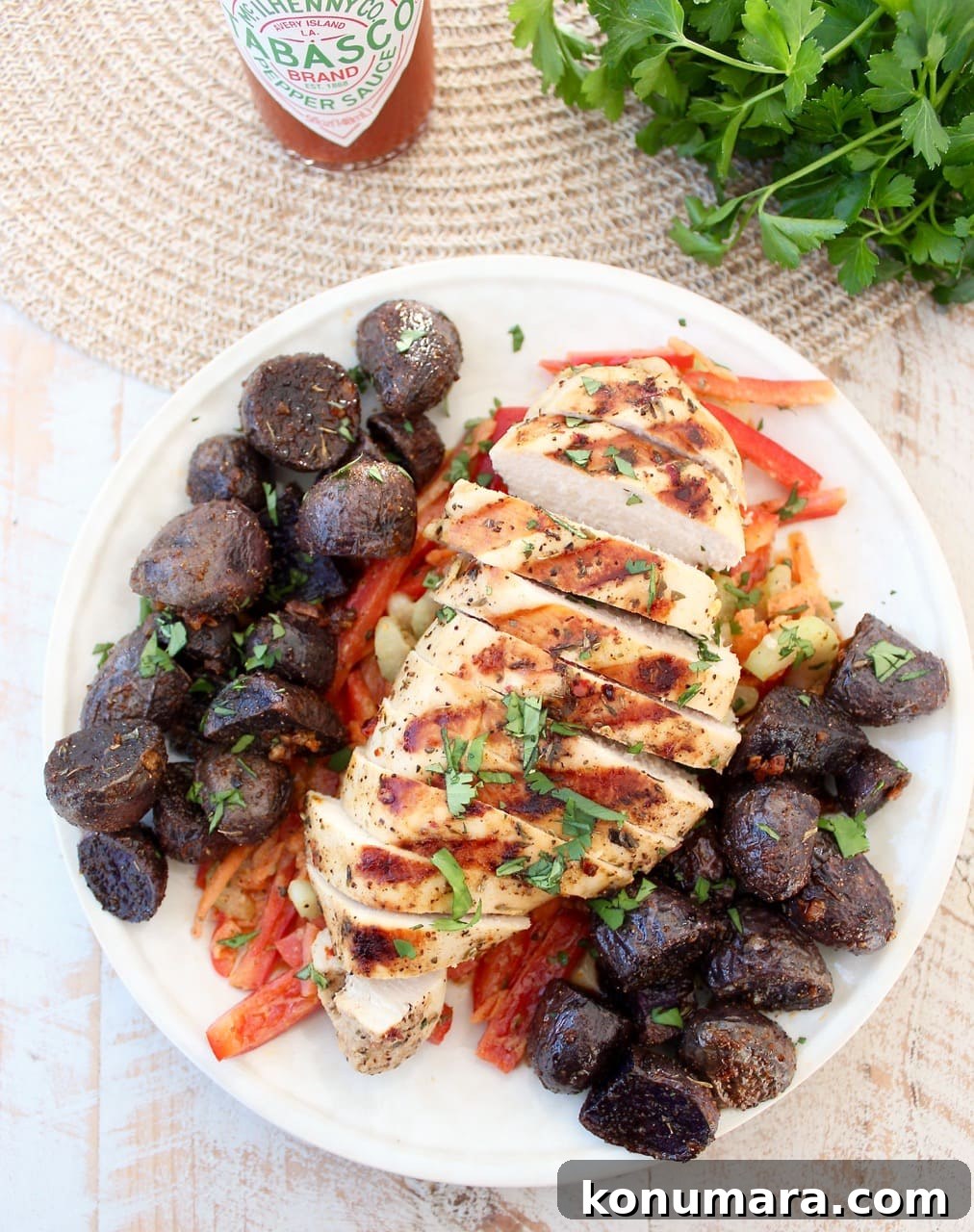 Sliced grilled chicken atop sliced bell peppers next to purple potatoes on a white plate.