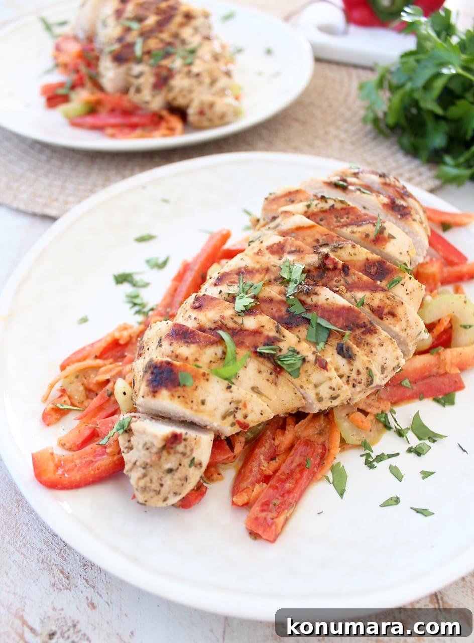 Sliced grilled chicken on sliced red peppers on a white plate.
