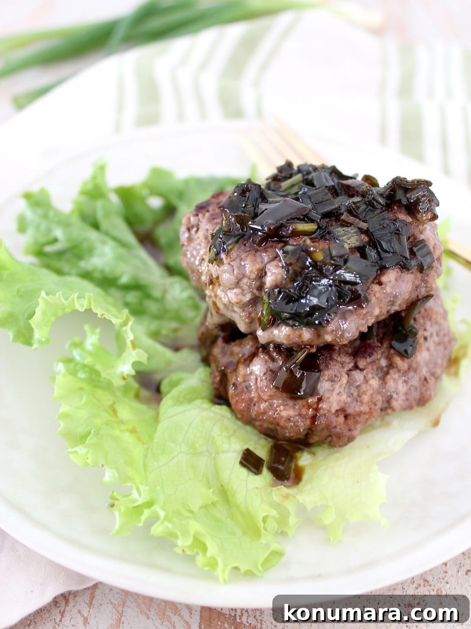 two cooked burger patties stacked on top of each other on a leaf of lettuce, topped with a scallion sauce