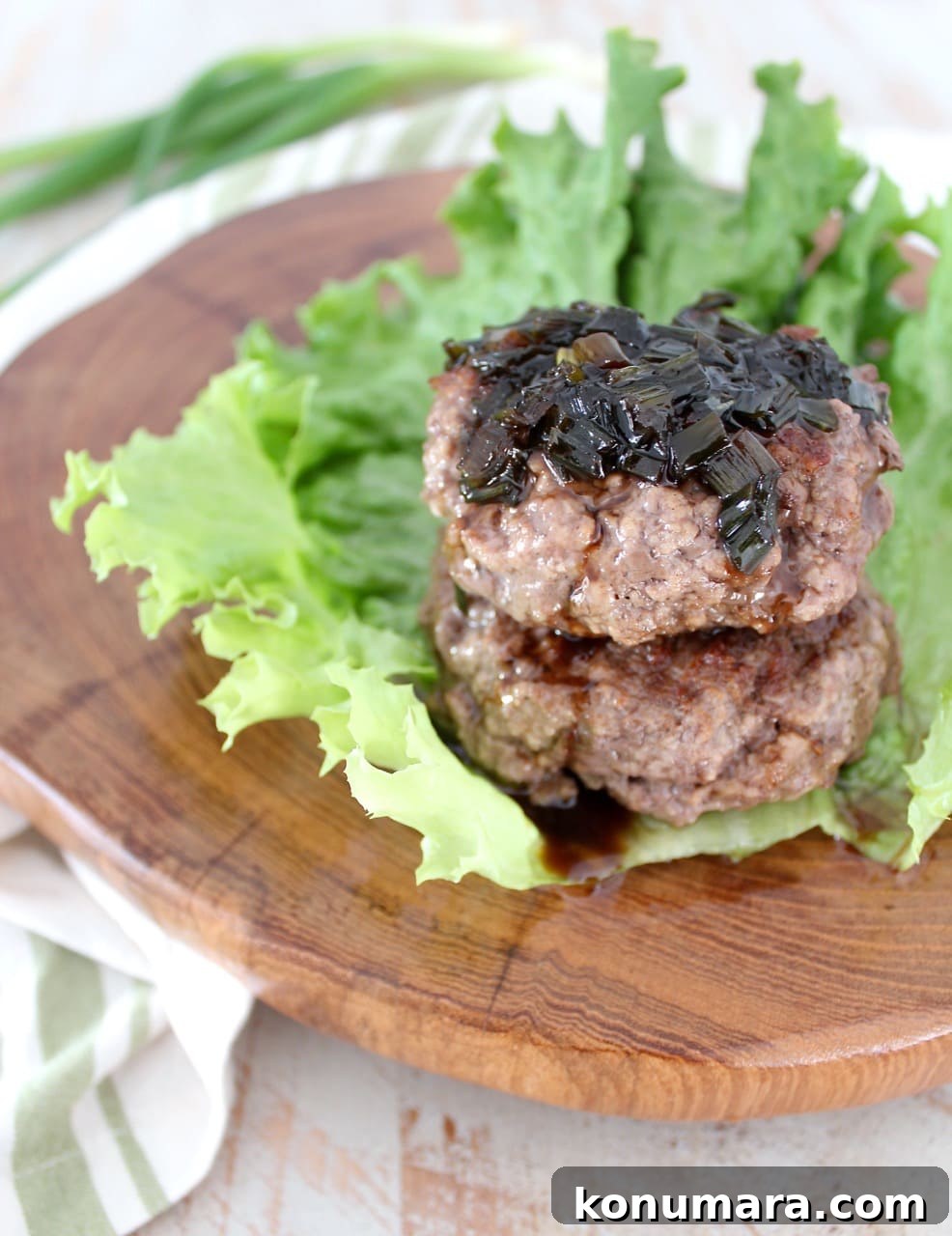 two cooked burger patties stacked on top of each other on a leaf of lettuce, topped with a scallion sauce