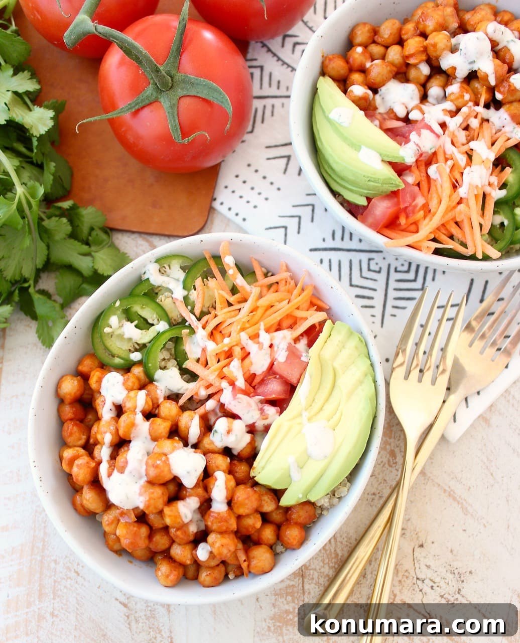 Spicy Vegan Buffalo Chickpea Buddha Bowl Recipe 2 bowls filled with chickpeas tossed in buffalo sauce and sliced vegetables with two forks on the side