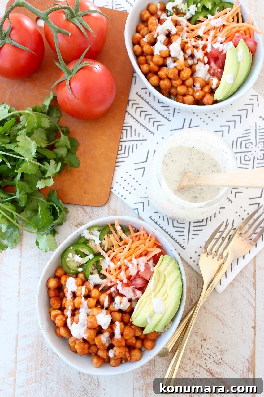 Spicy Vegan Buffalo Chickpea Buddha Bowl Recipe 4 bowls filled with chickpeas tossed in buffalo sauce and sliced vegetables with two forks and a jar of ranch dressing on the side
