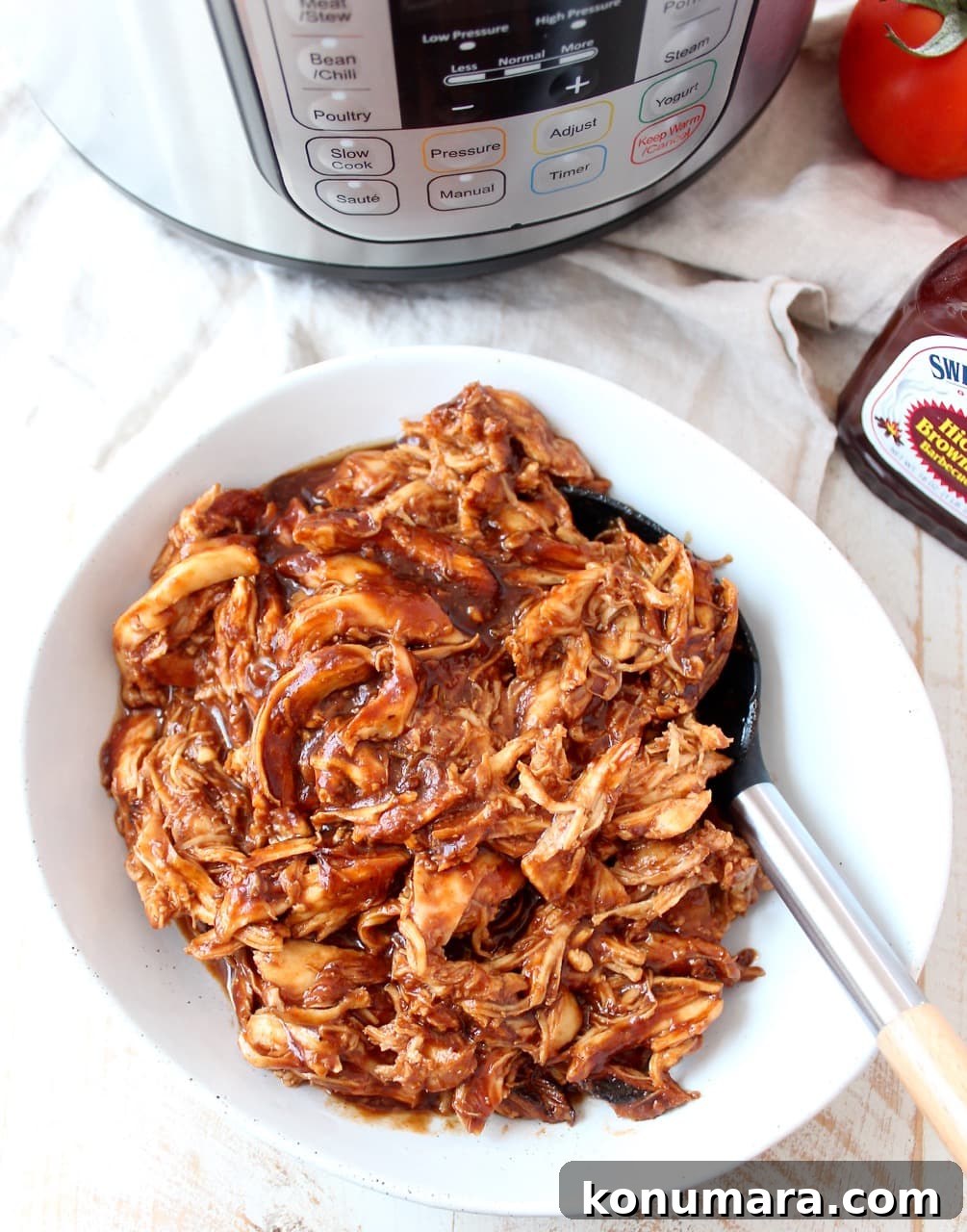 Smoky Instant Pot BBQ Chicken Recipe 2 Shredded chicken coated in BBQ sauce in a white bowl with a spoon.