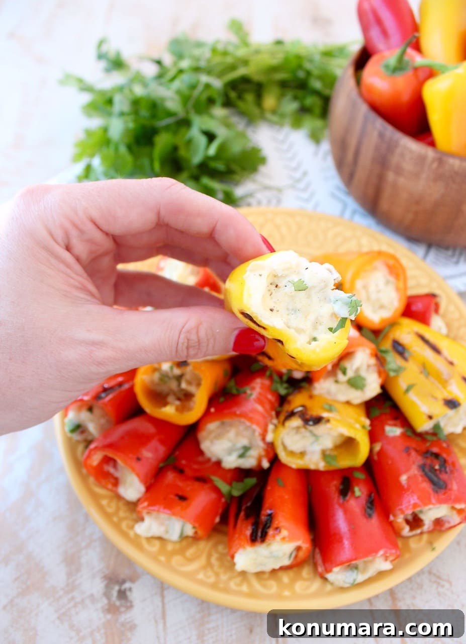 Grilled stuffed peppers are made with sweet mini peppers, filled with an easy, delicious creamy artichoke dip, creating the perfect appetizer for your next BBQ! Hand Holding Grilled Stuffed Peppers