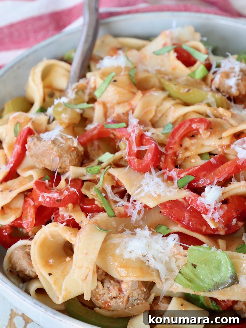 cooked pasta tossed with peppers, sausage and basil leaves in bowl with fork