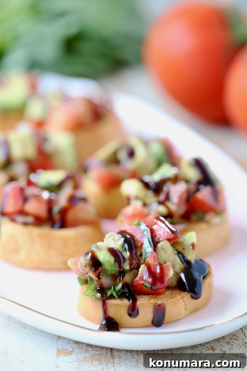 diced avocado and tomato on top of baguette slices on a plate with a drizzle of balsamic reduction on top