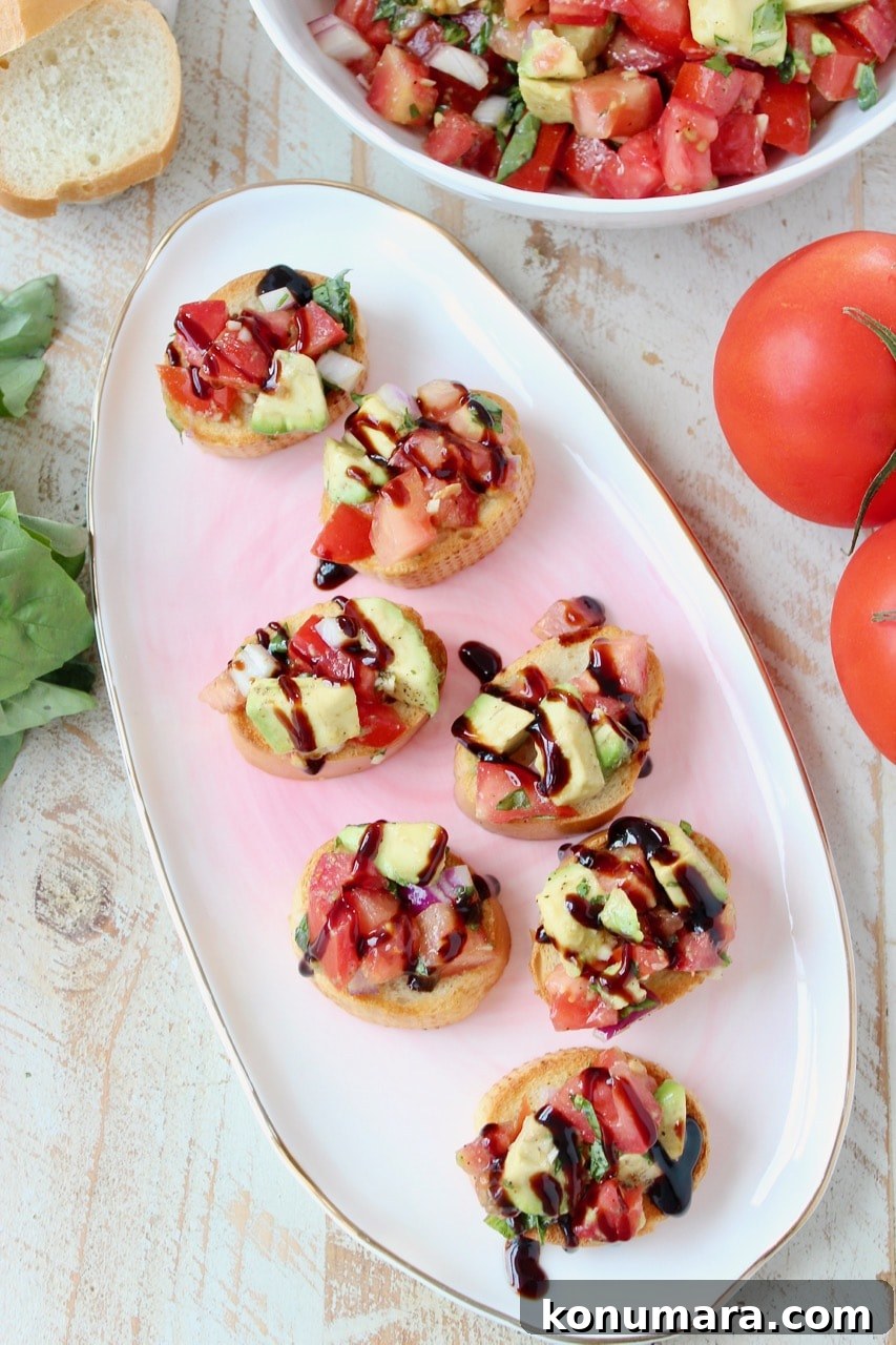 slices of a baguette on a plate topped with avocado bruschetta and balsamic reduction drizzled on top