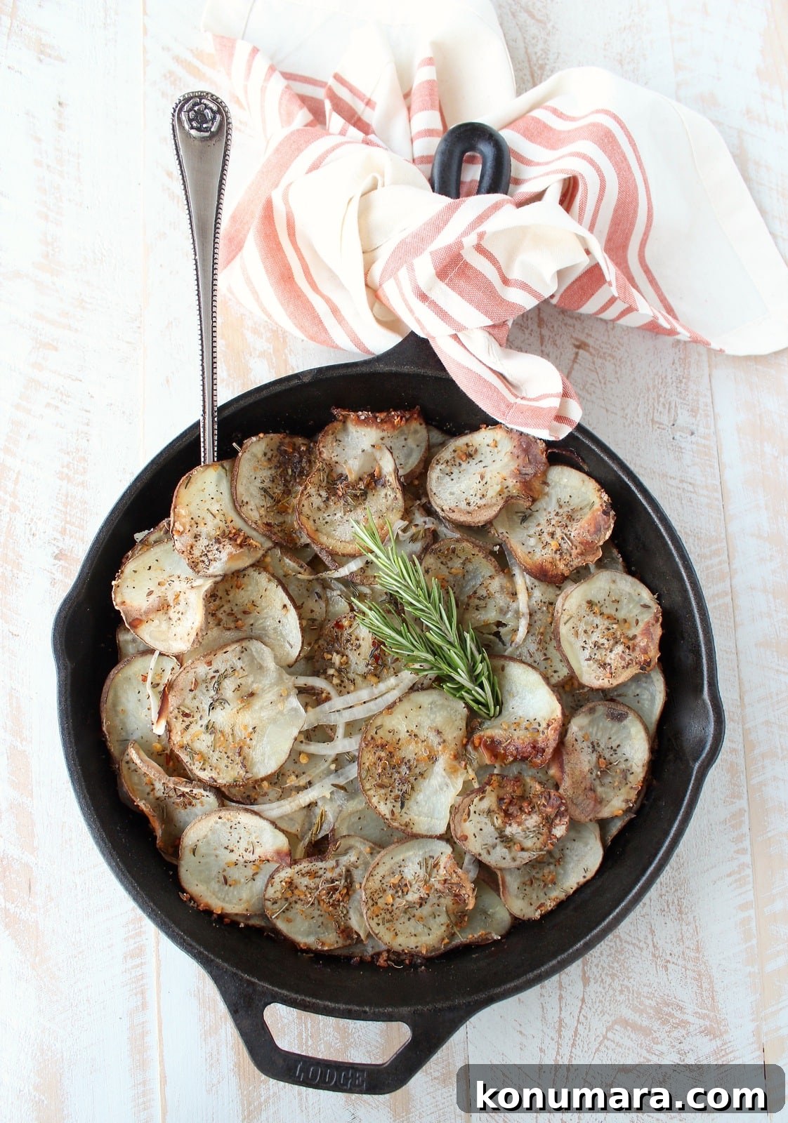 A cast iron skillet on a wooden surface filled with sliced and seasoned potatoes.
