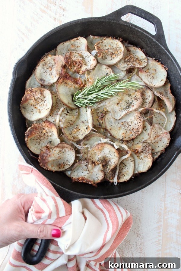 Hand holding a cast iron skillet over a wooden surface filled with sliced and seasoned potatoes.