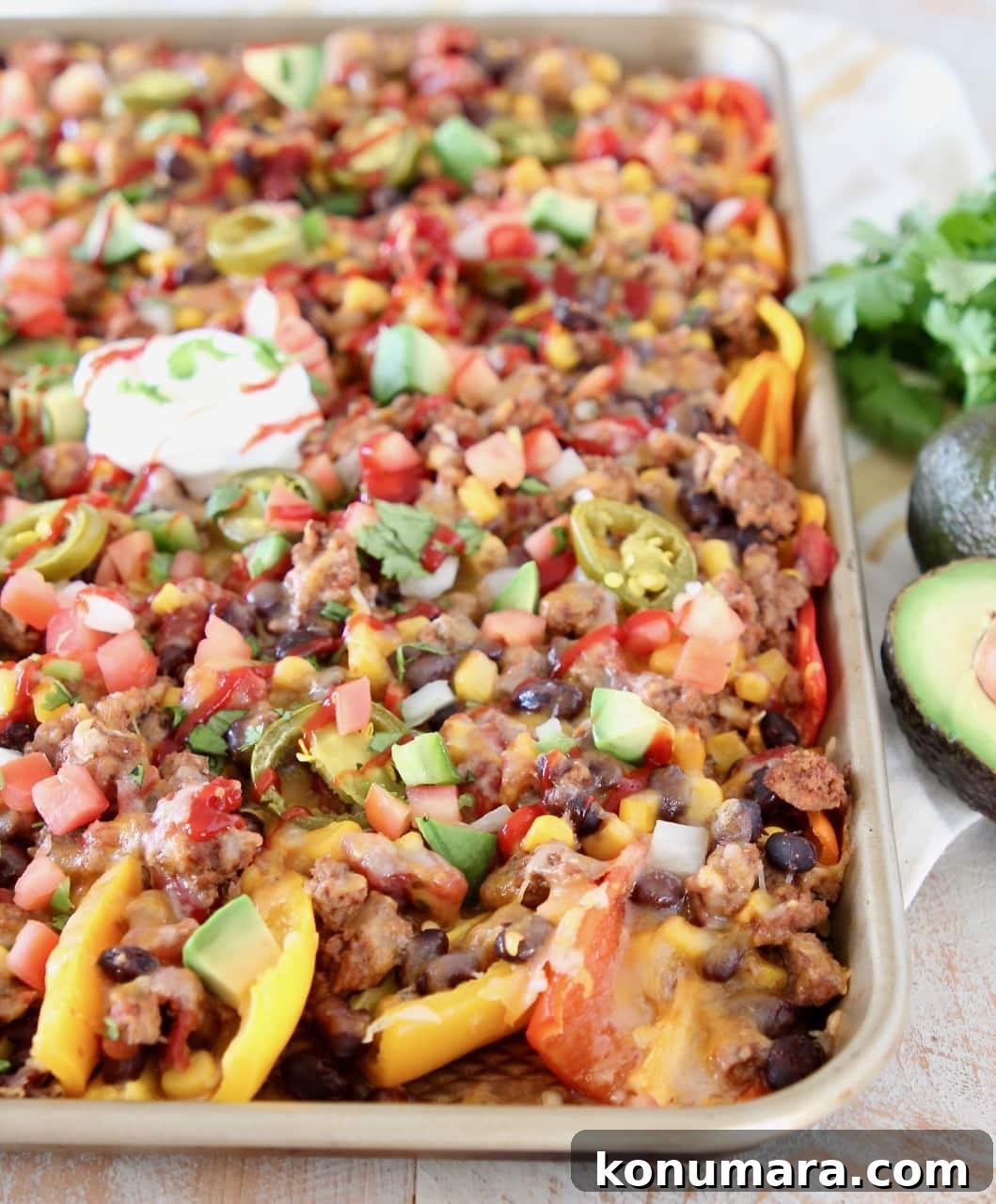 Mini peppers covered in cheese, beans, tomatoes, avocado and cilantro on sheet pan