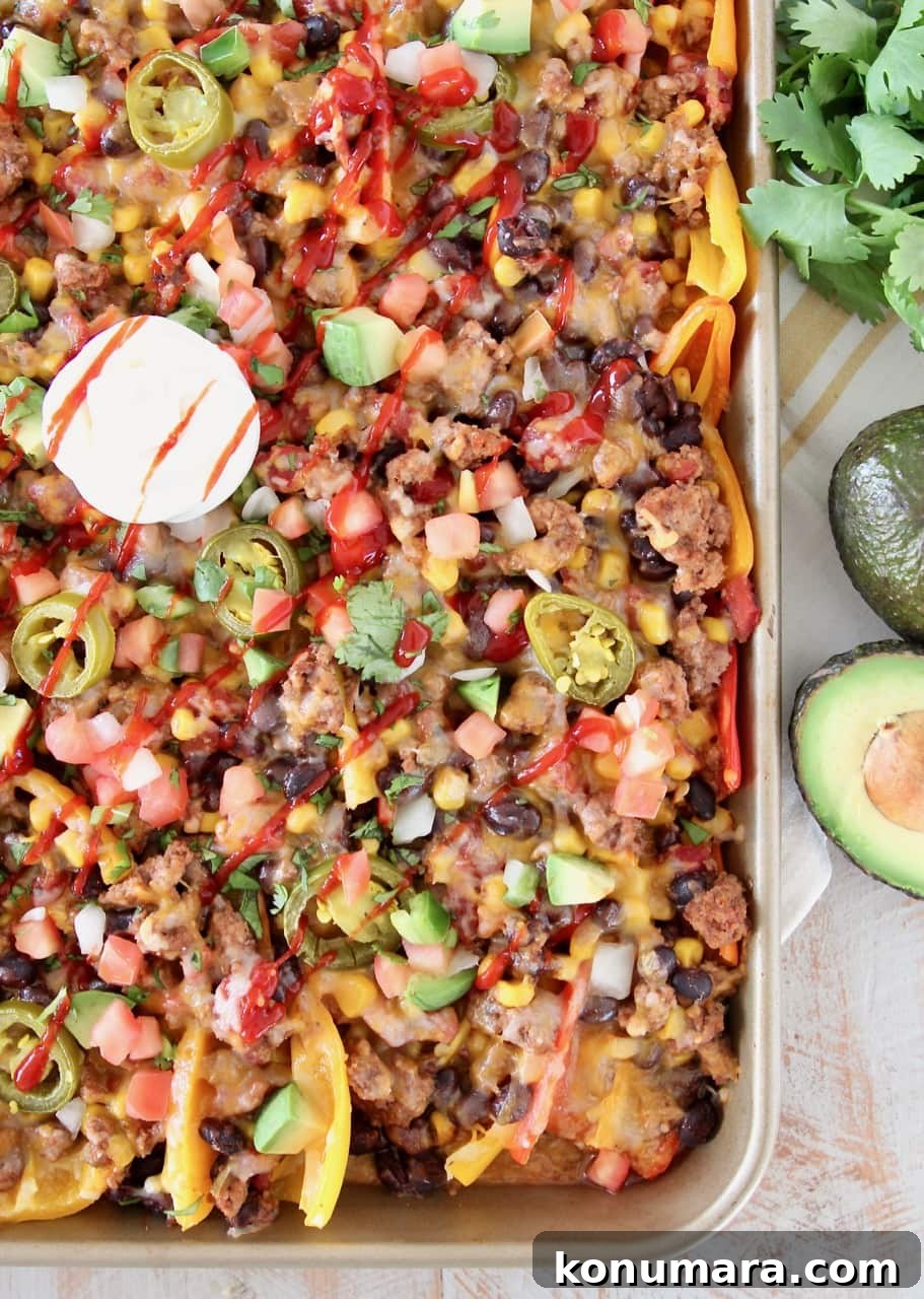 Low Carb Nachos made with sweet mini bell peppers, topped with turkey, beans, corn, tomatoes, jalapenos, avocado, hot sauce and sour cream on a baking sheet