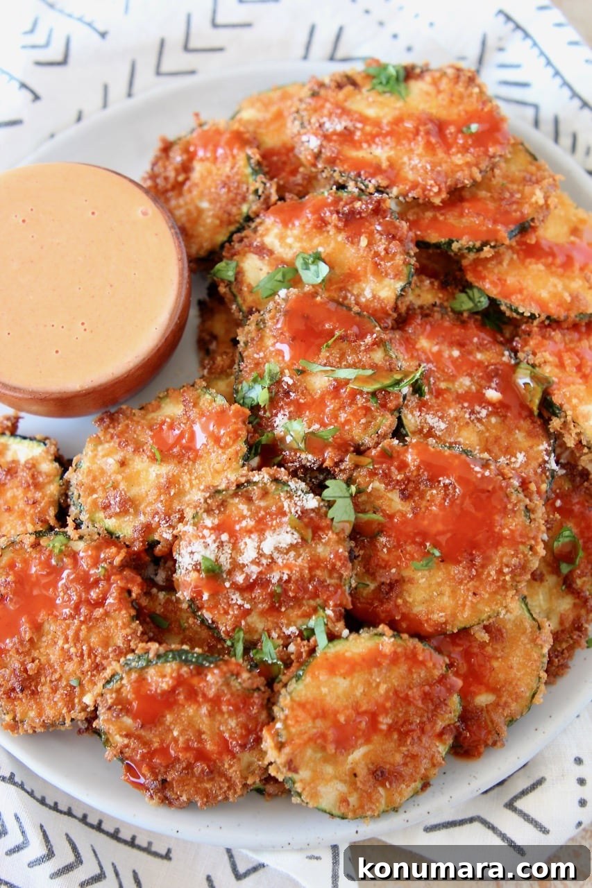 Crispy Zucchini Chips drizzled with buffalo sauce on plate with small bowl of buffalo blue cheese dressing