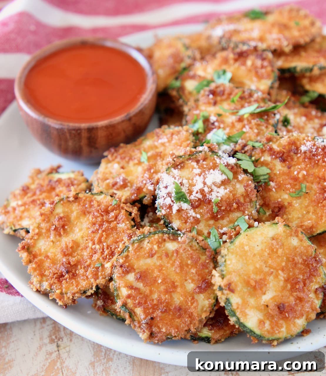 Crispy fried zucchini chips with parmesan cheese on a plate with small wooden bowl of buffalo sauce