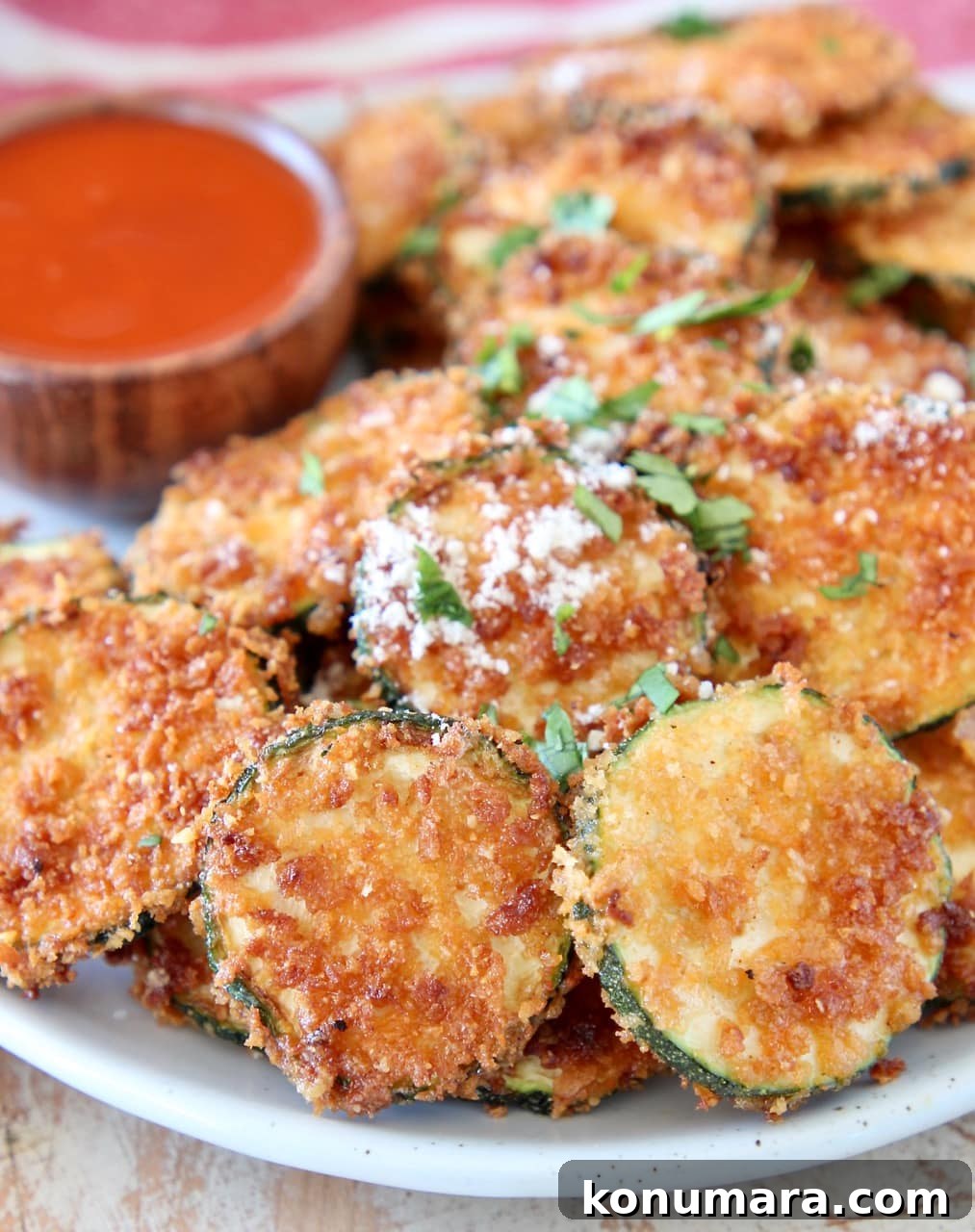 Crispy zucchini chips with parmesan cheese on plate with small bowl of buffalo sauce