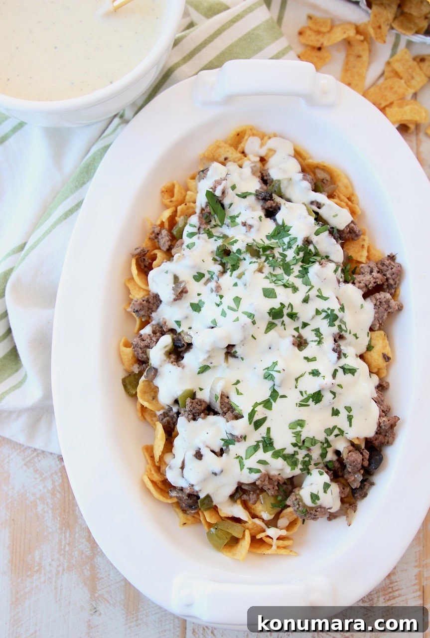 Philly cheesesteak frito chili pie in casserole dish covered with creamy provolone cheese sauce