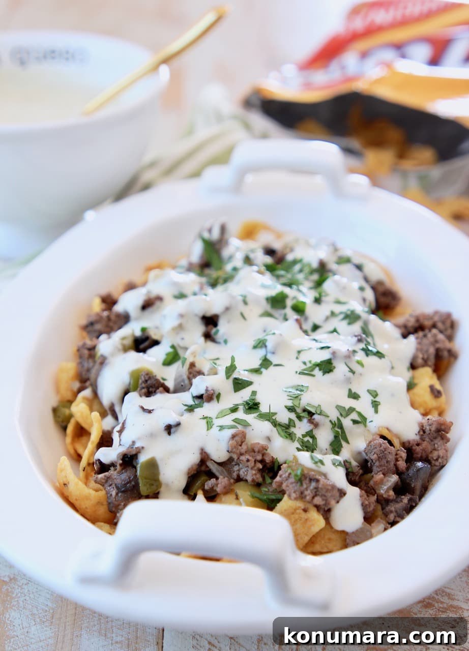 Philly Cheesesteak Frito Pie topped with Creamy Provolone Cheese Sauce in white casserole dish